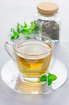 Herbal mint tea in glass cup with dry peppermint tea on background, vertical
