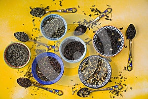Herbal and natural dry tea variation in bowls and vintage spoons on yellow background