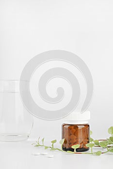 Herbal pills in glass bottle and green plant with glass of water on white background.