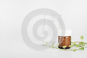 Herbal pills in glass bottle and green plant with glass of water on white background