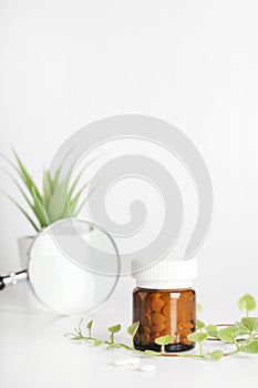 Herbal pills in glass bottle and magnifying glass near potted plant on white background