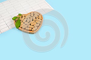 Herbal pills in heart shaped wooden plate and cardiogram on blue background.