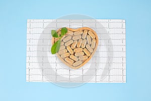 Herbal pills in heart shaped wooden plate and cardiogram on blue background.