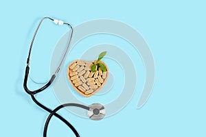 Herbal pills in heart shaped wooden plate and stethoscope on blue background.