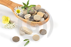 Herbal pills in a wooden spoon with fresh herbs and flowers for alternative medicine