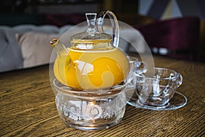 Herbal sea buckthorn tea in a transparent teapot and in a transparent glass with double heating bottom in restaurant. Concept of