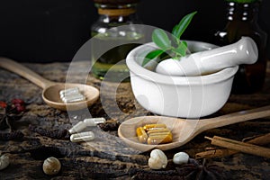 Herbal supplement in capsules on wooden spoon with healthy medicinal plant.