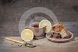 Herbal tea in a ceramic mug, honey in a plate and lemon on a wooden table. Still life