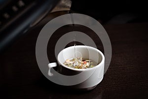 Herbal tea in a cup. Brewing a drink from different herbs in a white cup on a dark background