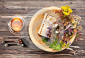 Herbal tea cup, healing herbs and honey in a wooden bowl on a wooden table.