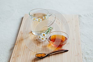 Herbal tea in glass cup with flowers of chamomile, turmeric and honey on a wooden board. Treatment hot drink. folk