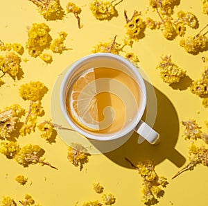 Herbal tea with immortelle and lemon in a white cup on a yellow background close up
