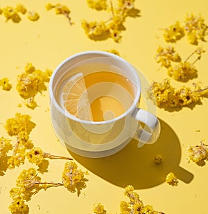 Herbal tea with immortelle and lemon in a white cup on a yellow background close up