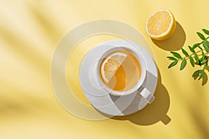 Herbal tea with lemon in a white cup on a yellow background with shadows