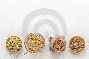 Herbal tea with pharmaceutical chamomile, dry chrysanthemum, a jar of dry rose petals and hunters on a white table