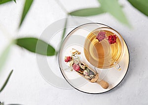 Herbal tea with pomegranate flowers in a glass cup on a plate on a white background with eucalyptus branches. The concept of a