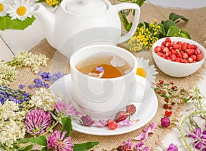 Herbal tea with rosehip, chamomile and clover in a white cup on a wooden table with flowers
