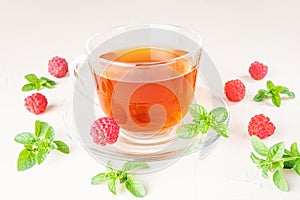 Herbal tea in a transparent cup with a saucer on a light background.