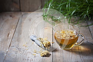 Herbal tea in a transparent glass mug with calendula flowers on a wooden background. Phytotea