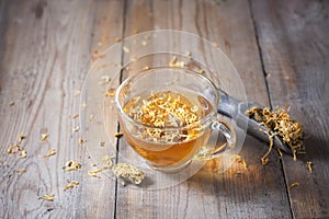 Herbal tea in a transparent glass mug with calendula flowers on a wooden background. Phytotea