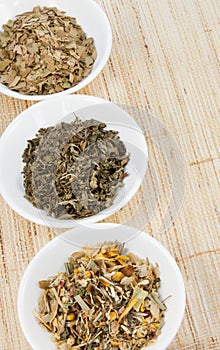 Herbal teas in small white bowls on natual matting