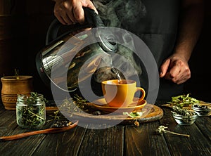 An herbalist pours boiling water into a mug to brew healthy tea on the table. Traditional medicine concept or making medicinal tea