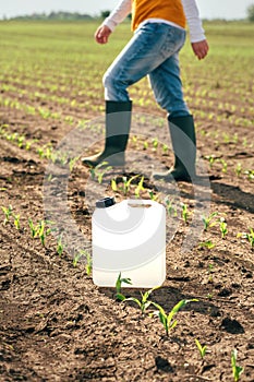 Herbicide jug container in corn seedling field, farmer walking in background