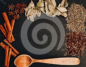 Herbs in kitchen, frame of spices, cinnamon sticks, star anise, wooden spoon, Various spices on stone black table