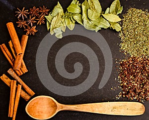 Herbs in kitchen, frame of spices, cinnamon sticks, star anise, wooden spoon, Various spices on stone black table