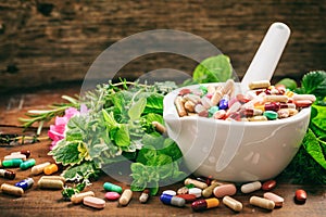 Herbs and pills in a mortar on wooden background