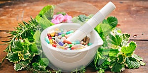 Herbs and pills in a mortar on wooden background