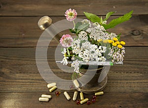 Herbs and a thermometer in a copper mortar and pestle, capsules and pills scattered around