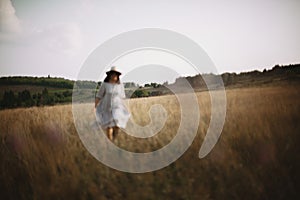 Herbs and wildflowers in sunny meadow in mountains and blurred image of girl in linen dress walking. Boho woman relaxing in