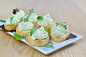 Herded cream cheese with arugula canapes on white plate