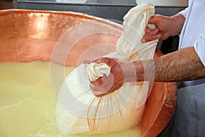 Herdsman Cheesemaker collects cheese from the copper cauldron w