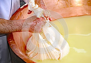 Herdsman Cheesemaker collects cheese from the copper cauldron w