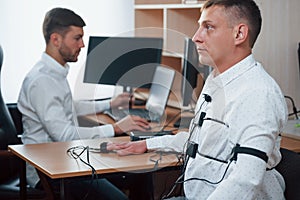 Here nobody condemns anyone, don`t worry. Suspicious man passes lie detector in the office. Asking questions. Polygraph photo