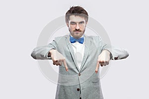 Here and right now. Portrait of serious bossy handsome bearded man in casual grey suit and blue bow tie standing pointing and