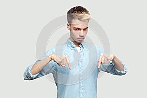 Here and right now. Portrait of serious handsome young man in light blue shirt standing, pointing his finger down, looking at