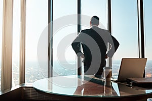 Here to dominate in the business game. Rearview shot of a young businessman looking out the window in an office.