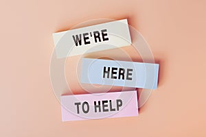 WE ARE HERE TO HELP. Concept of text on color cards. Top view image of cards and on pastel beige background