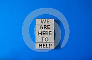 We are here to help symbol. Concept words we are here to help on wooden blocks. Beautiful blue background. Business and we are