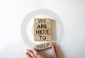 We are here to help symbol. Concept words we are here to help on wooden blocks. Beautiful blue background. Businessman hand.