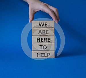 We are here to help symbol. Concept words we are here to help on wooden blocks. Beautiful blue background. Businessman hand.