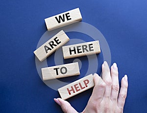 We are here to help symbol. Concept words we are here to help on wooden blocks. Beautiful deep blue background. Businessman hand.
