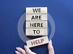 We are here to help symbol. Concept words we are here to help on wooden blocks. Beautiful deep blue background. Businessman hand.