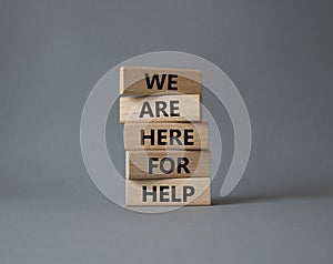 We are here to help symbol. Concept words we are here to help on wooden blocks. Beautiful grey background. Business and we are