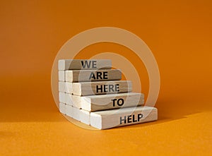 We are here to help symbol. Concept words we are here to help on wooden blocks. Beautiful orange background. Business and we are
