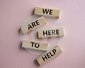 We are here to help symbol. Concept words we are here to help on wooden blocks. Beautiful pink background. Business and we are