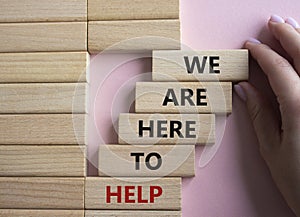 We are here to help symbol. Concept words we are here to help on wooden blocks. Beautiful pink background. Businessman hand.